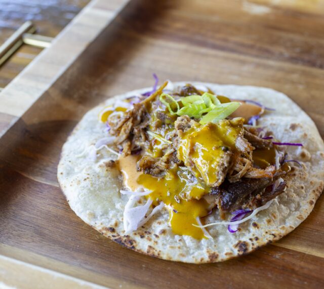 A flour tortilla with cabbage, smoked pulled pork, Cajun coleslaw sauce, North and South Carolina BBQ sauce, and green onion.